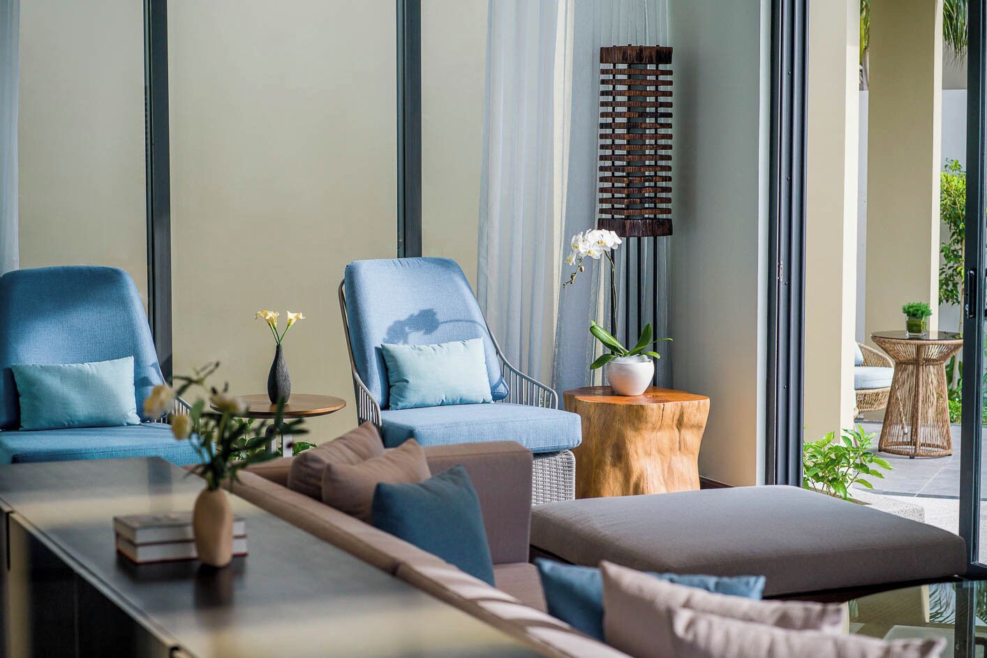 A modern lounge area with two blue armchairs, a wooden side table, and a sofa.