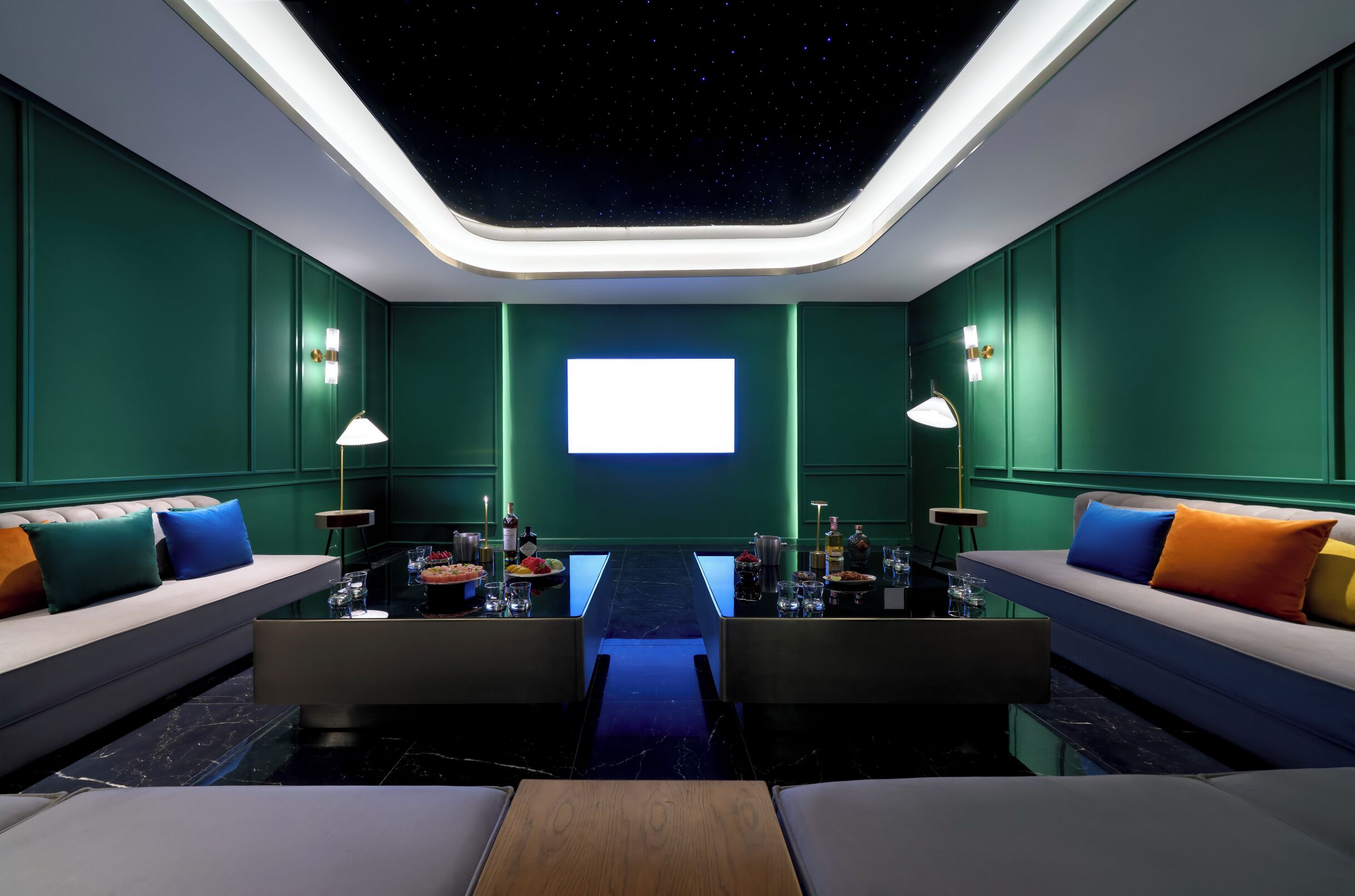 A modern room with a starry ceiling, green walls, and a central table with seating on either side.