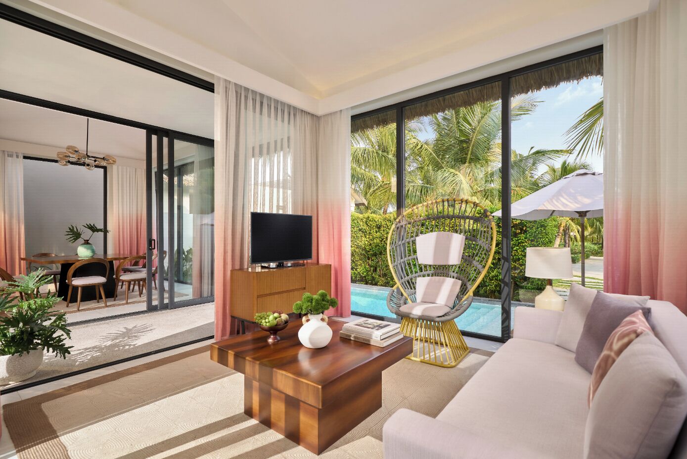 A modern hotel room with a large window, a television, a sofa, a dining area, and a pool view.