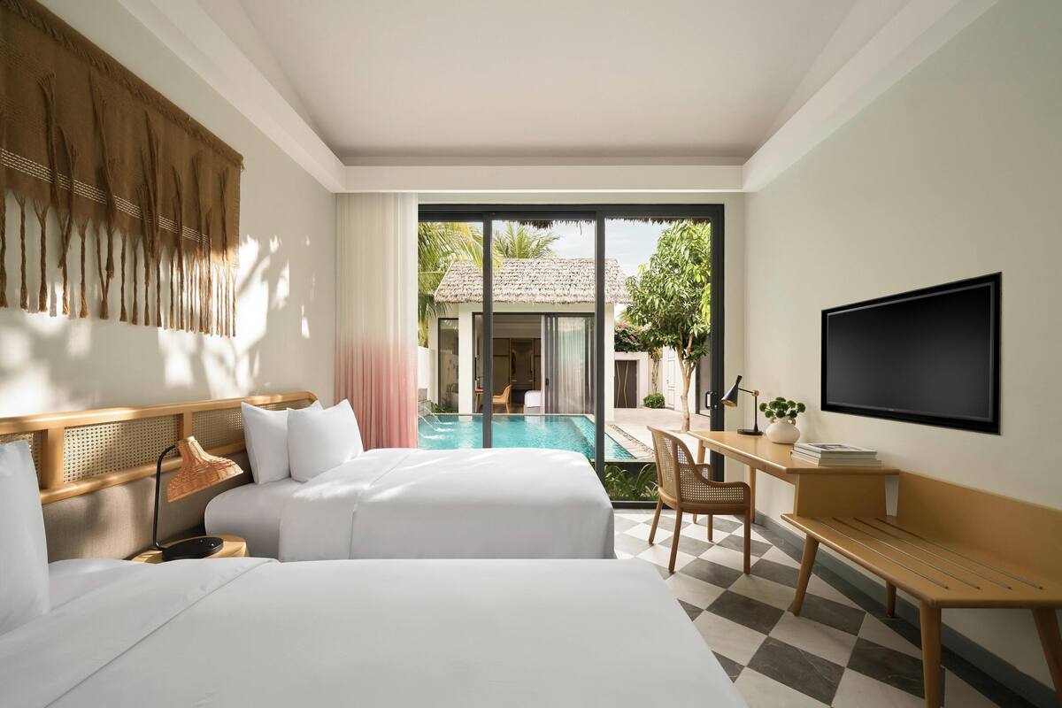 A hotel room with two beds, a desk, a TV, and a view of a pool and outdoor area.