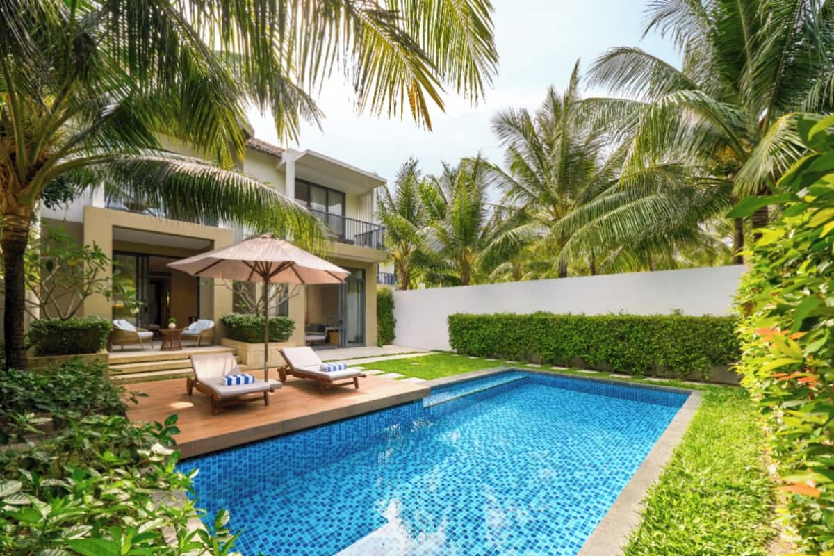 A swimming pool with lounge chairs and an umbrella, surrounded by palm trees and greenery.