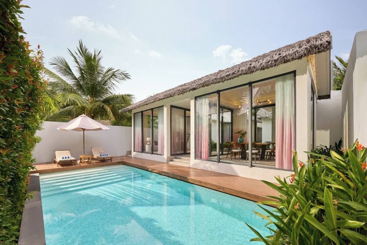 A modern poolside area with a clear pool, lounge chairs, and a glass-enclosed patio.
