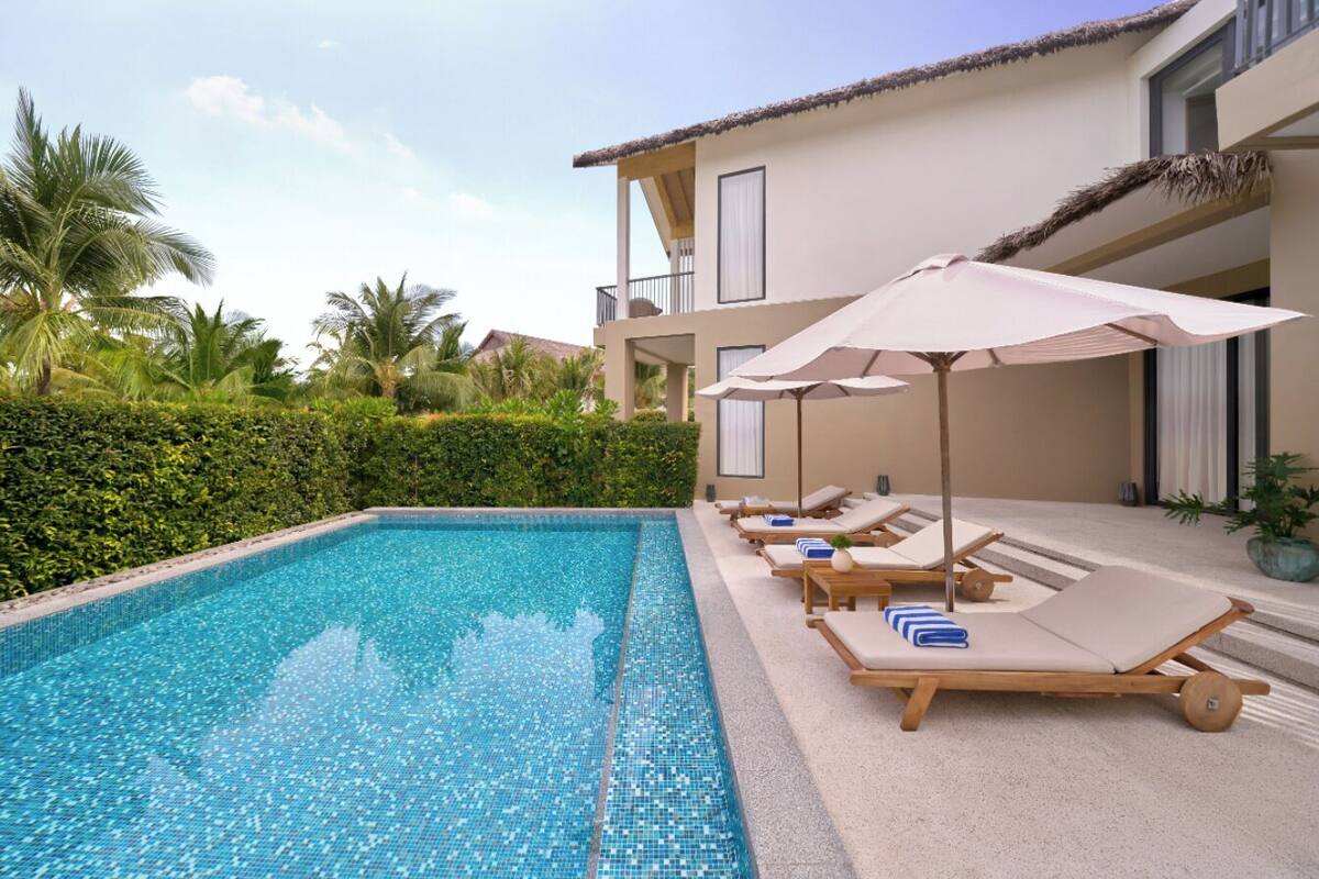 A pool area with lounge chairs and umbrellas, surrounded by a hedge and palm trees.