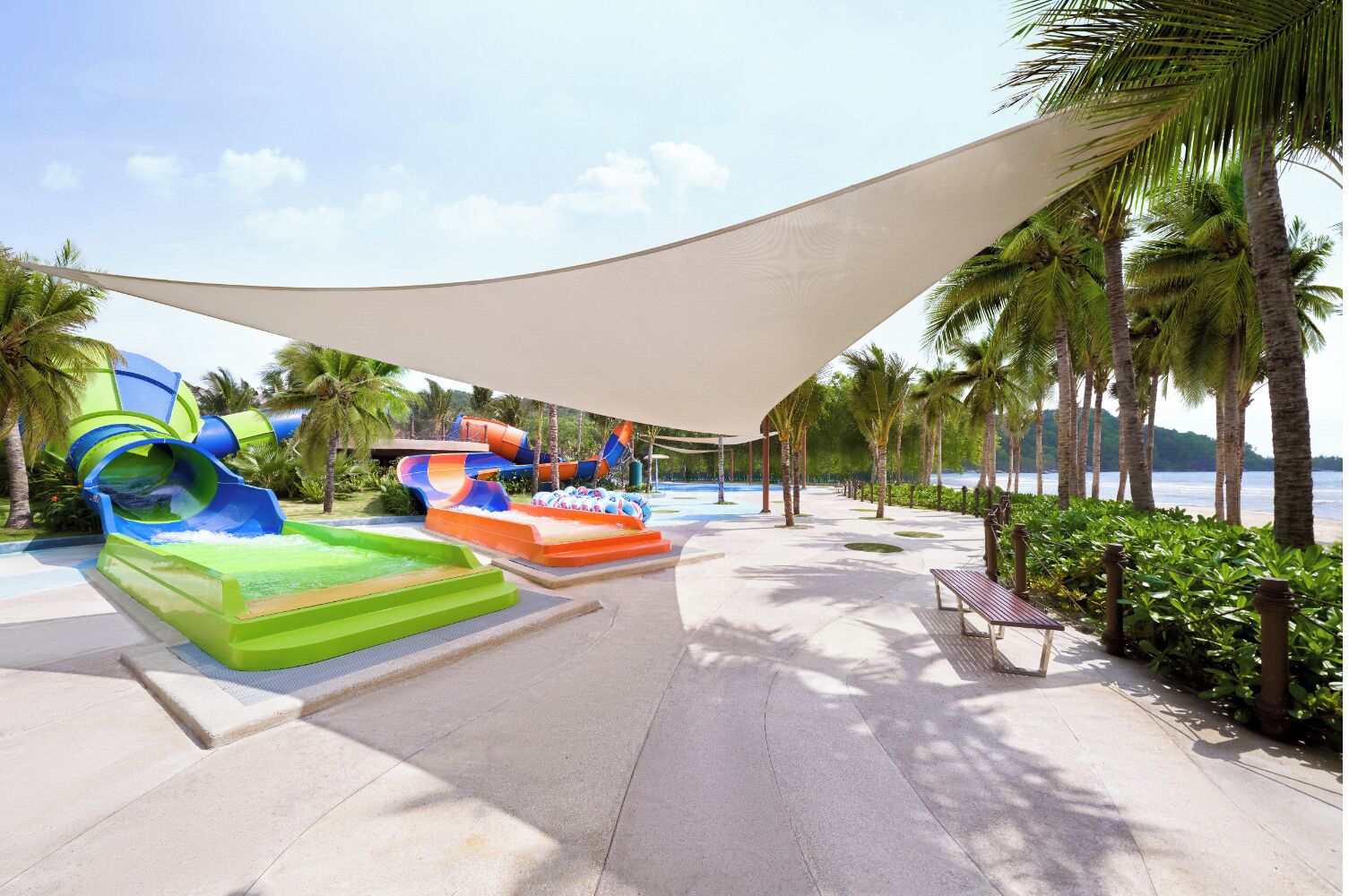 A water park with slides and inflatable rafts, surrounded by palm trees and a beach.