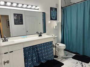 Un baño con tocador blanco, un espejo grande, un inodoro y una cortina de ducha azul.