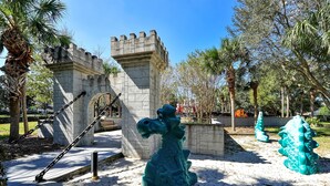 Ein Park mit einem steinernen Torbogen, einer Drachenstatue und einem schlossartigen Gebäude.