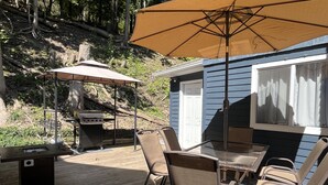 Une terrasse avec un barbecue, des chaises et un parasol.