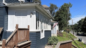 Une maison à deux étages avec un porche à l’avant, un escalier en bois et un petit jardin devant.