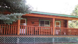 A wooden cabin with a porch, a lattice fence, and a green lawn.