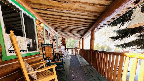 A wooden deck with a railing, rocking chairs, and a view of trees.