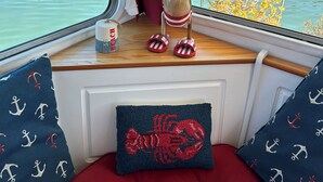Et bådeinteriør med udsigt til en havn, en flaske og slippers på en vindueskarm.
