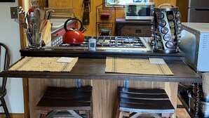 Une cuisine avec des meubles de rangement en bois, une cuisinière à gaz, une bouilloire et une machine à café.