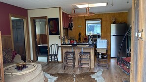 Une cuisine chaleureuse avec des meubles en bois, un tabouret de bar et un réfrigérateur.