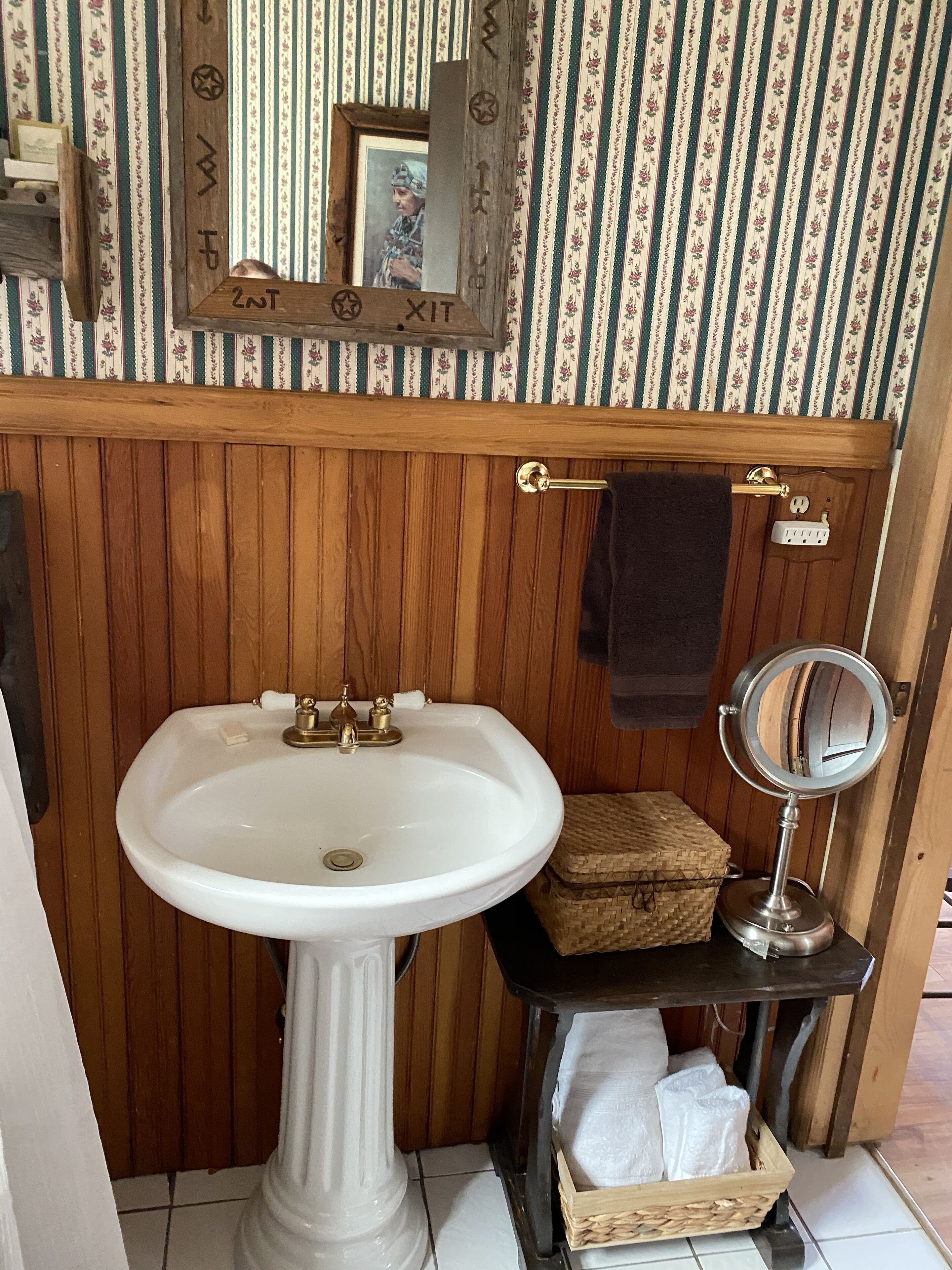 Un baño con lavamanos pedestal, tocador de madera, espejo y barra para toallas.