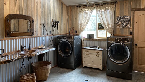 Une buanderie avec des murs en bois, deux machines à laver, un évier et un miroir.