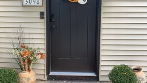 Eine schwarze Haustür mit Halloween-Dekoration, einer Hausnummer und einer Fußmatte.
