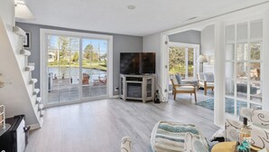 Ein geräumiges Wohnzimmer mit großem Fernseher, Kamin und Blick auf eine Terrasse und einen Außenbereich.