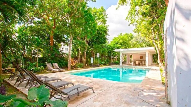A swimming pool surrounded by lush greenery, with lounge chairs and a covered seating area.