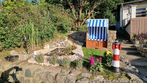 Ein Garten mit kleinem Pool, einer Holzbank, einem Schild für die Sauna und einem roten und weißen Leuchtturmmodell.
