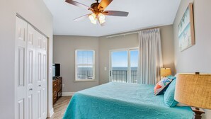 Ein Schlafzimmer mit Bett, Deckenventilator, Fernseher, Kommode und Meerblick durch eine Schiebetür.