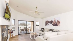 A spacious living room with a white sofa, a coffee table, a fireplace, and a ceiling fan. - Western Hills-Pool Heat Avail- Putting Green-Games (Fountain Hills)