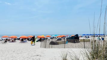 A beach with rows of sun loungers and umbrellas, a wooden fence, and a clear sky.