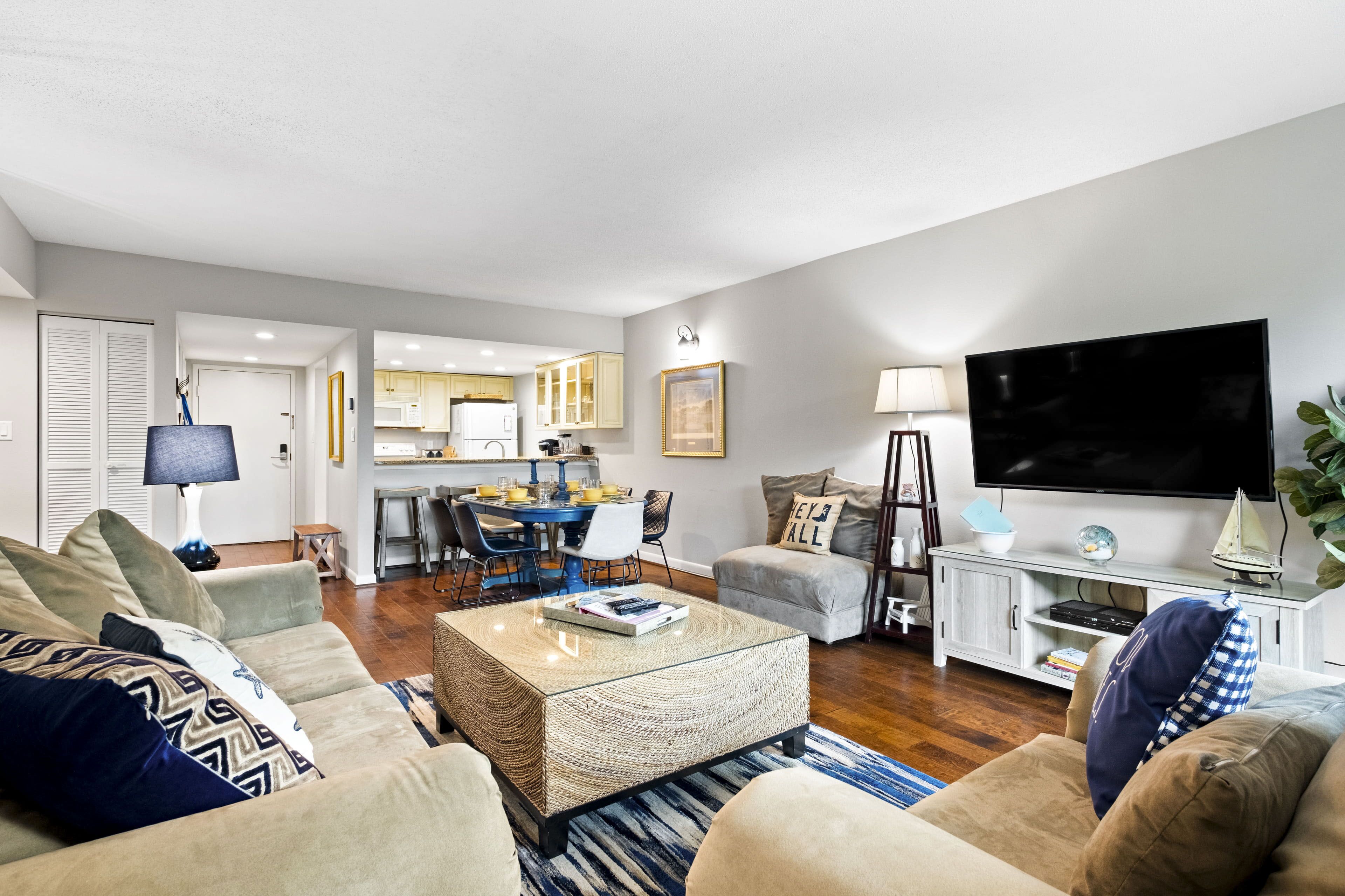 A modern living room with a sofa, coffee table, and TV. There is a kitchen area in the background.