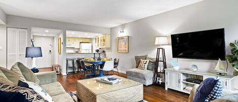 A modern living room with a sofa, coffee table, and TV. There is a kitchen area in the background.
