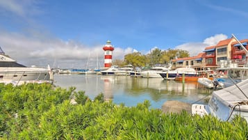 A marina with boats docked, a lighthouse, and a building with balconies.
