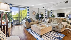 A spacious living room with a large sofa, a coffee table, and a balcony with a view of greenery. - Relax By Pool: Harbour Town Resort Condo (Hilton Head Island)