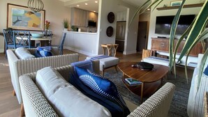 A modern living room with wicker furniture, a wooden coffee table, and a dining area with blue chairs.
