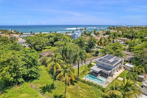 Zona residencial con una casa moderna, techo con paneles solares, piscina y vista al océano.