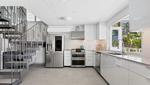 A modern kitchen with stainless steel appliances, white cabinetry, and a staircase with geometric design. - Your own beach house, private pool & pickle ball court, steps to beach.  (Sabana, Vega Alta, Puerto Rico)