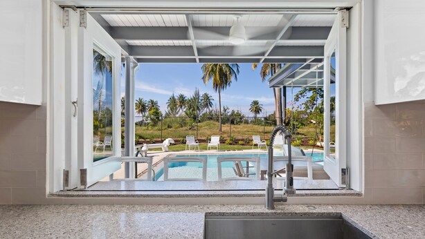 A kitchen with a view of a pool and palm trees. - Your own beach house, private pool & pickle ball court, steps to beach.  (Sabana, Vega Alta, Puerto Rico)