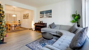 A modern living room with a grey sofa, a coffee table, a piano, a dining area with a Christmas tree, and a painting on the wall. - Spacious Thornton Home: 15 Mi to Downtown Denver! (Thornton)