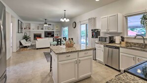 A modern kitchen with white cabinetry, granite countertops, and stainless steel appliances. There is a dining area with a white table and chairs, and a living room with a white sofa and a ceiling fan. - Spacious Thornton Home: 15 Mi to Downtown Denver! (Thornton)