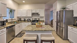 A modern kitchen with white cabinets, stainless steel appliances, granite countertops, and a central island with two stools. - Spacious Thornton Home: 15 Mi to Downtown Denver! (Thornton)