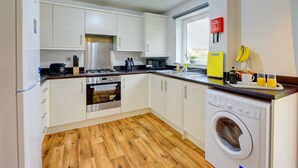 Una cocina moderna con armarios blancos, un refrigerador de acero inoxidable, un microondas y una lavadora.