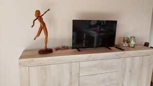 Ein HolztV-Möbel mit einem Flachbildfernseher, einer Fernbedienung und dekorativen Gläsern.