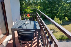 Un balcon avec une table et une chaise en bois, un vase avec une fleur et une vue sur un paysage verdoyant.