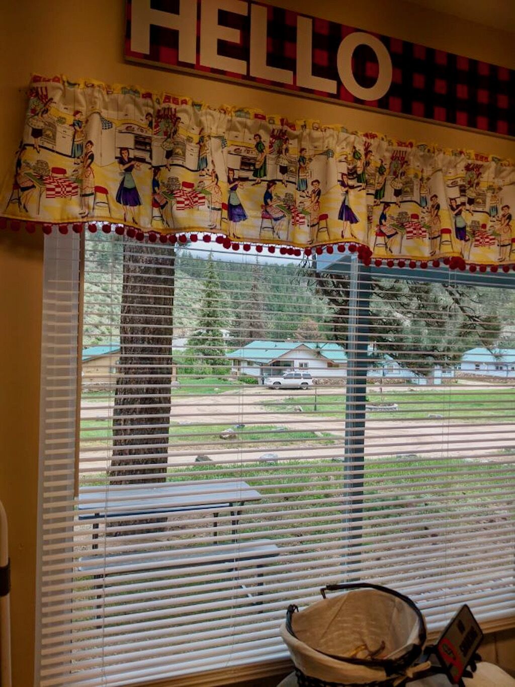 A room with a large window, a 'HELLO' sign above, and a colorful curtain with a kitchen scene.