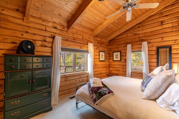 A wooden cabin bedroom with a bed, a dresser, and a ceiling fan.