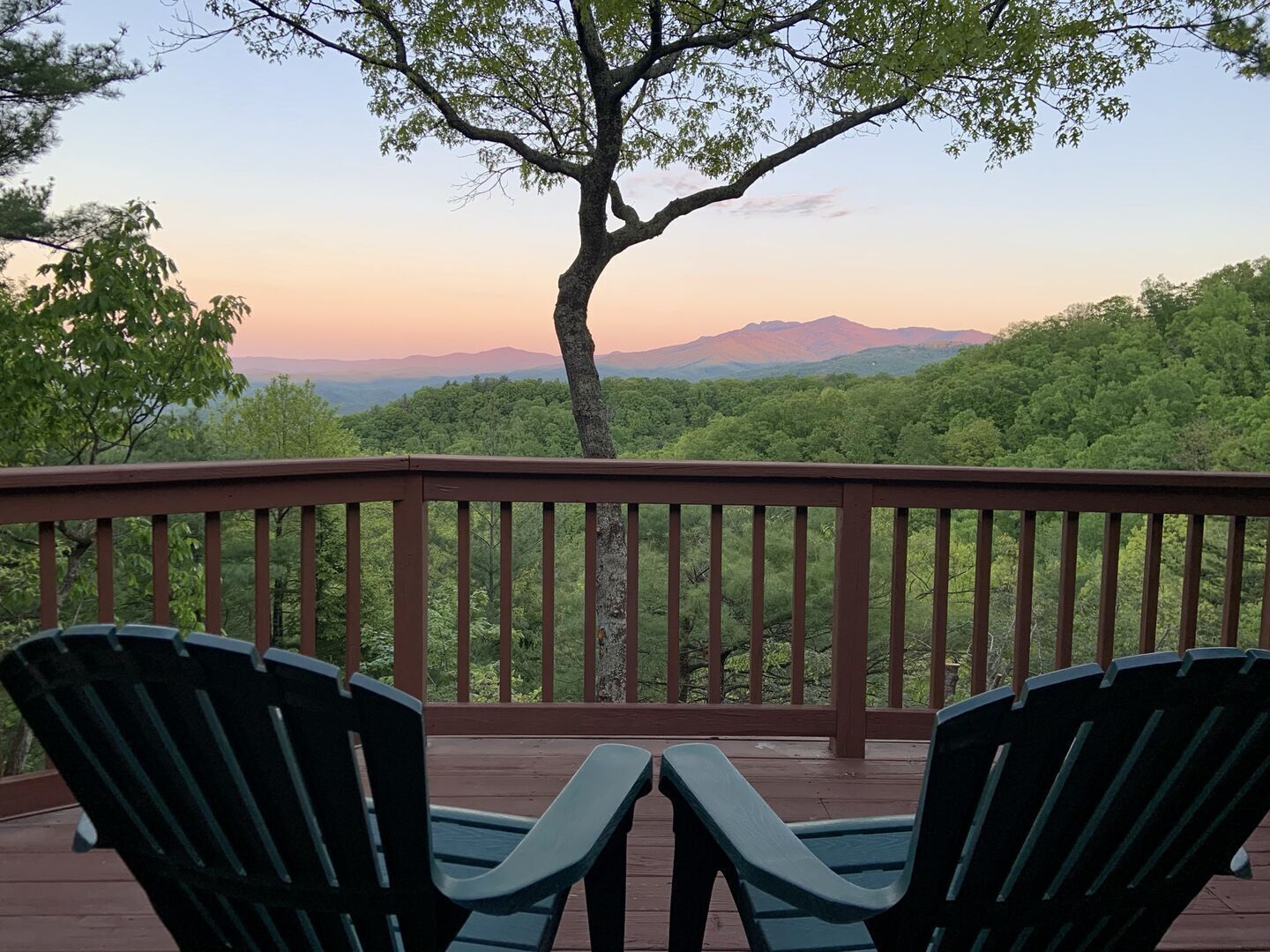 A deck with two Adirondack chairs overlooking a forested landscape with distant mountains.