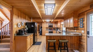 Una cocina de estilo cabaña con isla central, armarios de madera y una escalera que sube a un dormitorio tipo loft.
