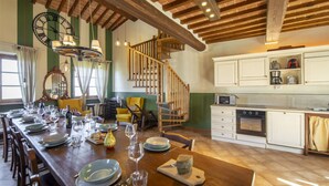 A spacious dining area with a long wooden table set for a meal, a kitchen with white cabinets, and a wooden staircase leading to an upper level. - La Smarrita by Interhome (Lucignano)