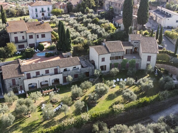 A large, historic building with multiple wings, surrounded by olive groves and a swimming pool.