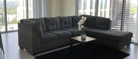 A modern living room with a grey sectional sofa, a black rug, and a ceiling fan.