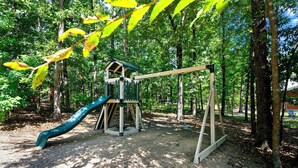 Ein Spielplatz mit Rutsche und Schaukeln in einem bewaldeten Gebiet.