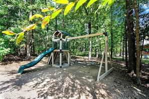 A playground with a slide and swings in a wooded area. - Coyote Creek: 3 bedroom, 3.5 bath sleeps 11 (Broken Bow)