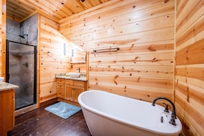 A wooden cabin bathroom with a freestanding bathtub, a shower, and wooden cabinets.